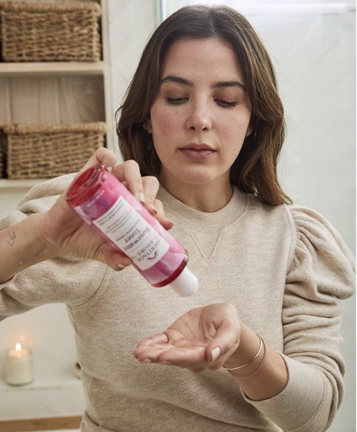 A person pouring out rosewater toner in the palm of her hand