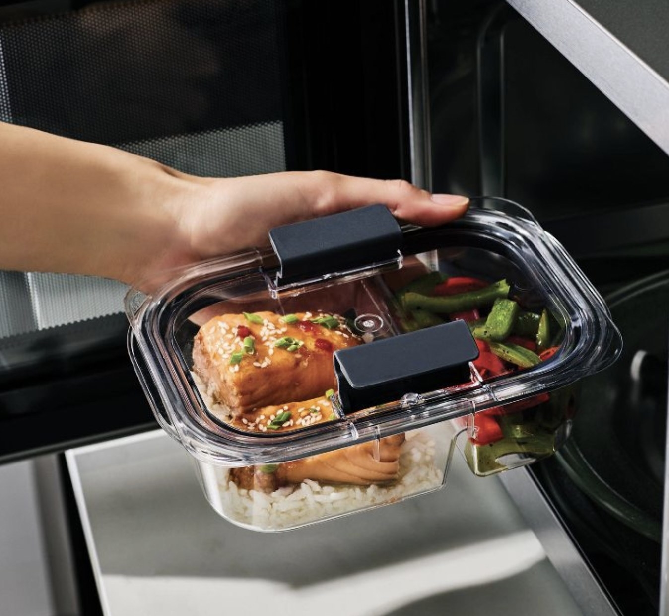 A hand holding a clear meal prep container