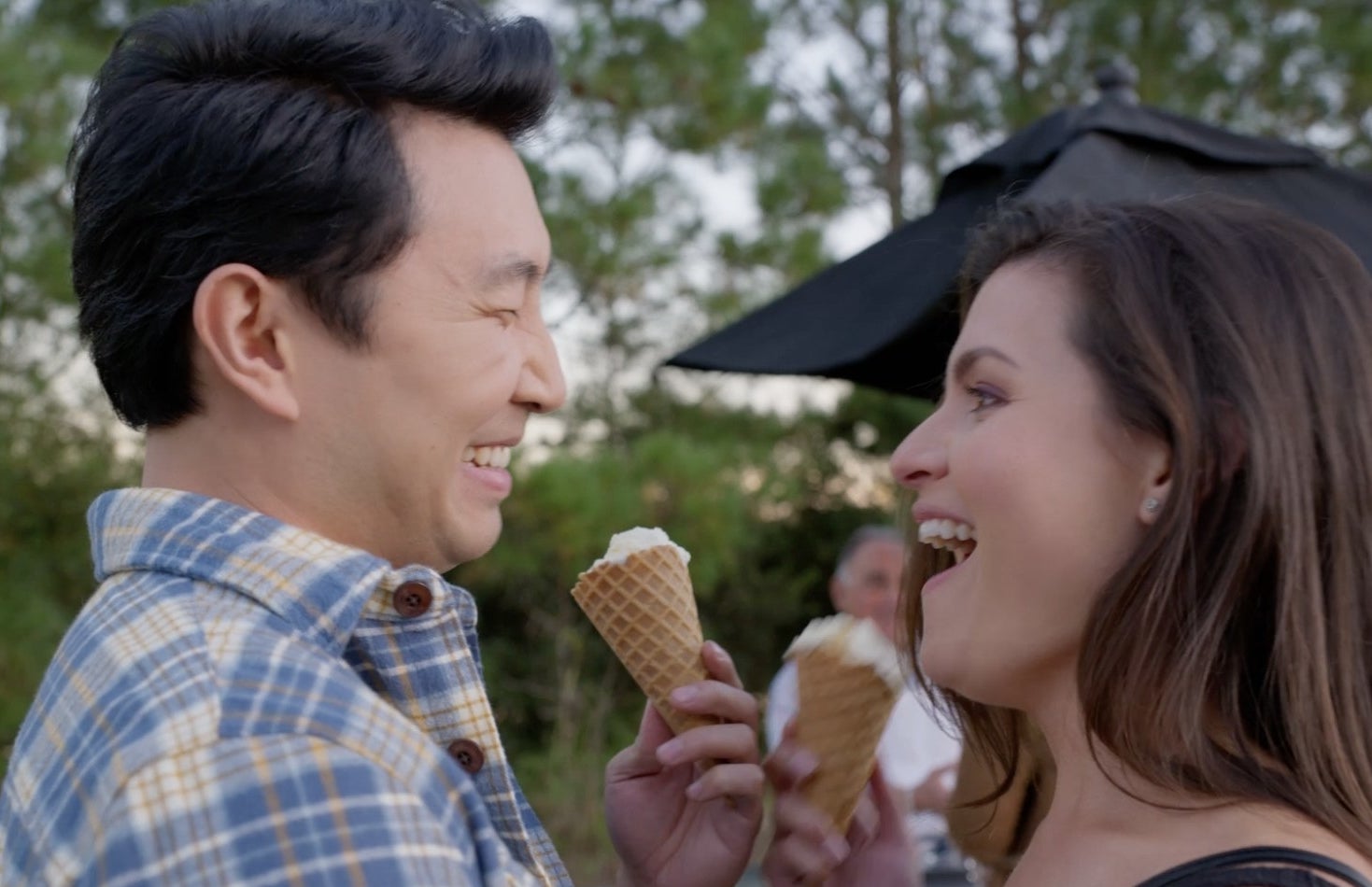 A man and a woman share ice cream cones, laughing.