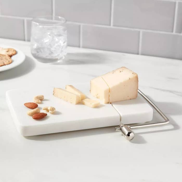 A rectangular cutting board with a cheese slicer on one end