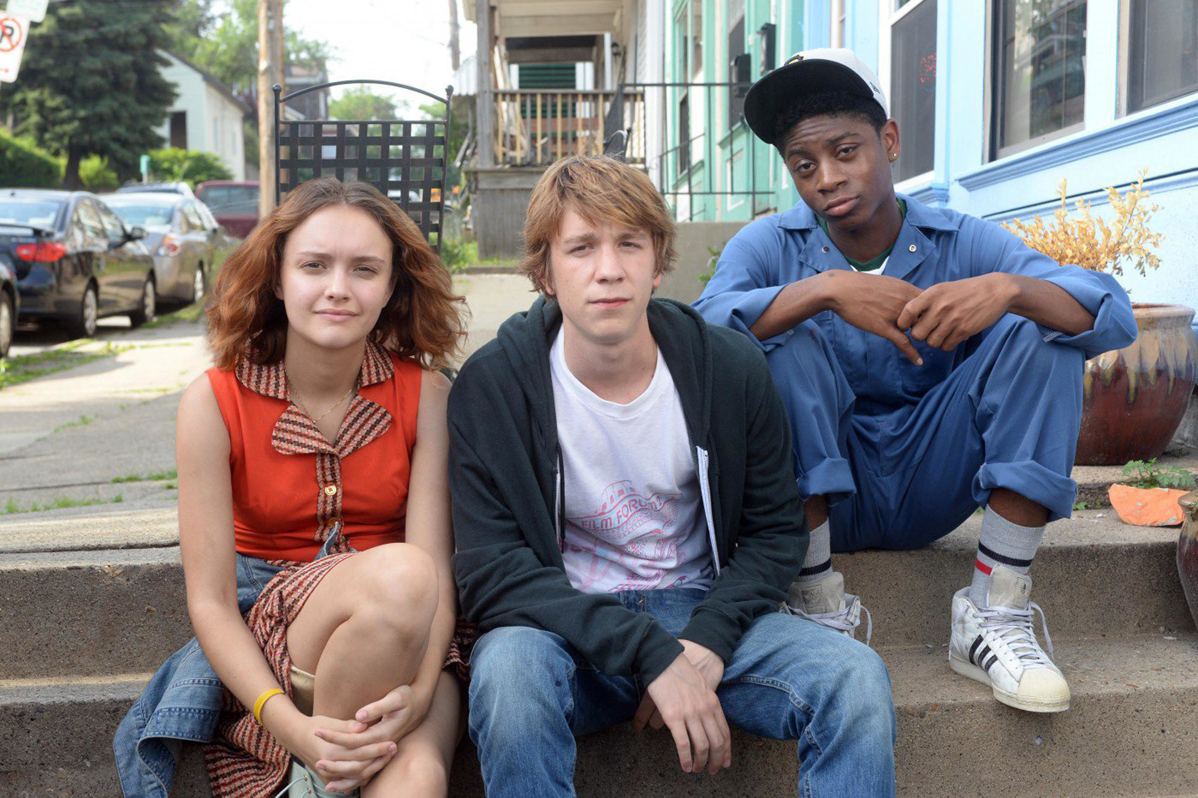 Three teenagers sitting on a sidewalk pose for a picture