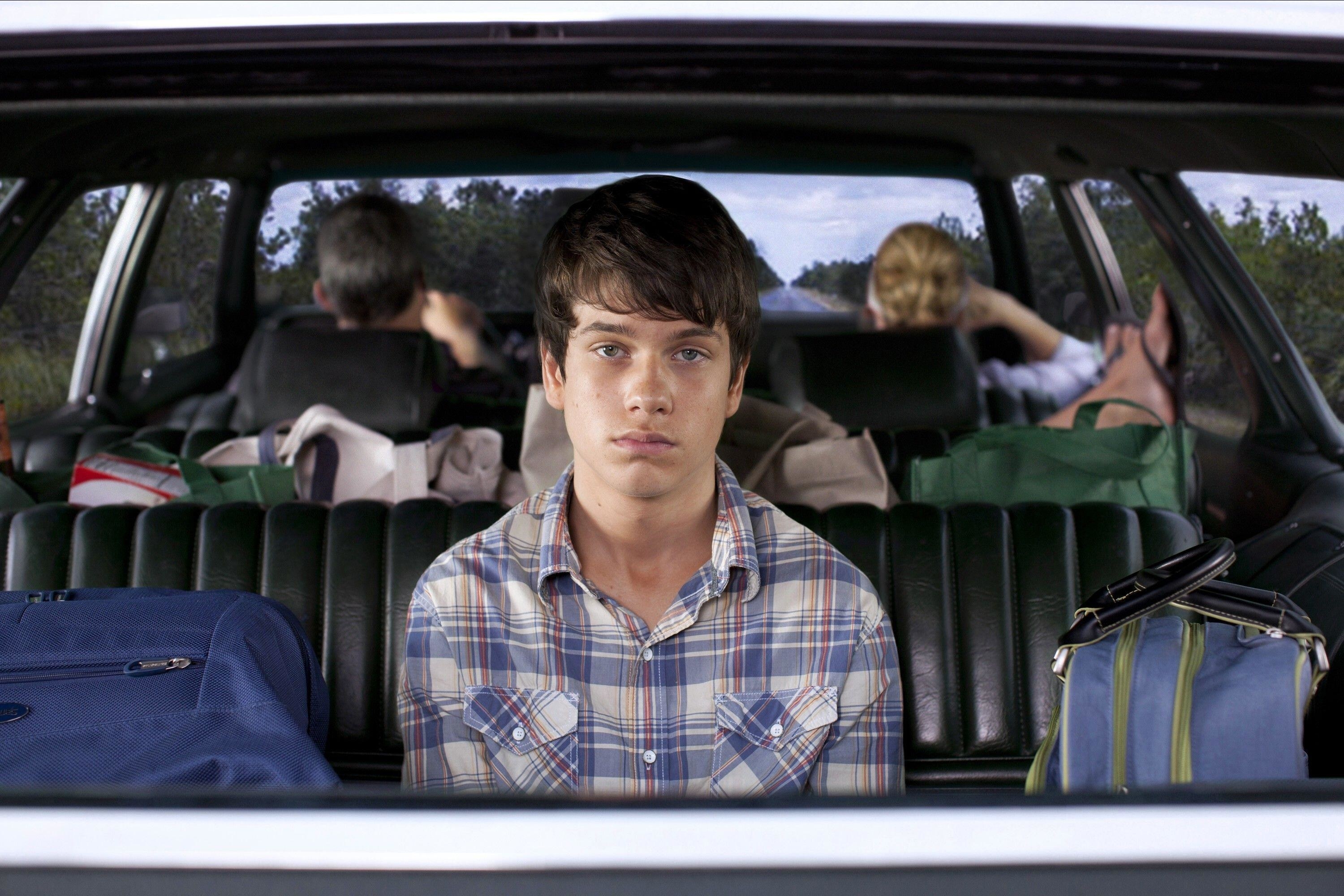 A young man stares despondently out of the rear window of his family&#x27;s car