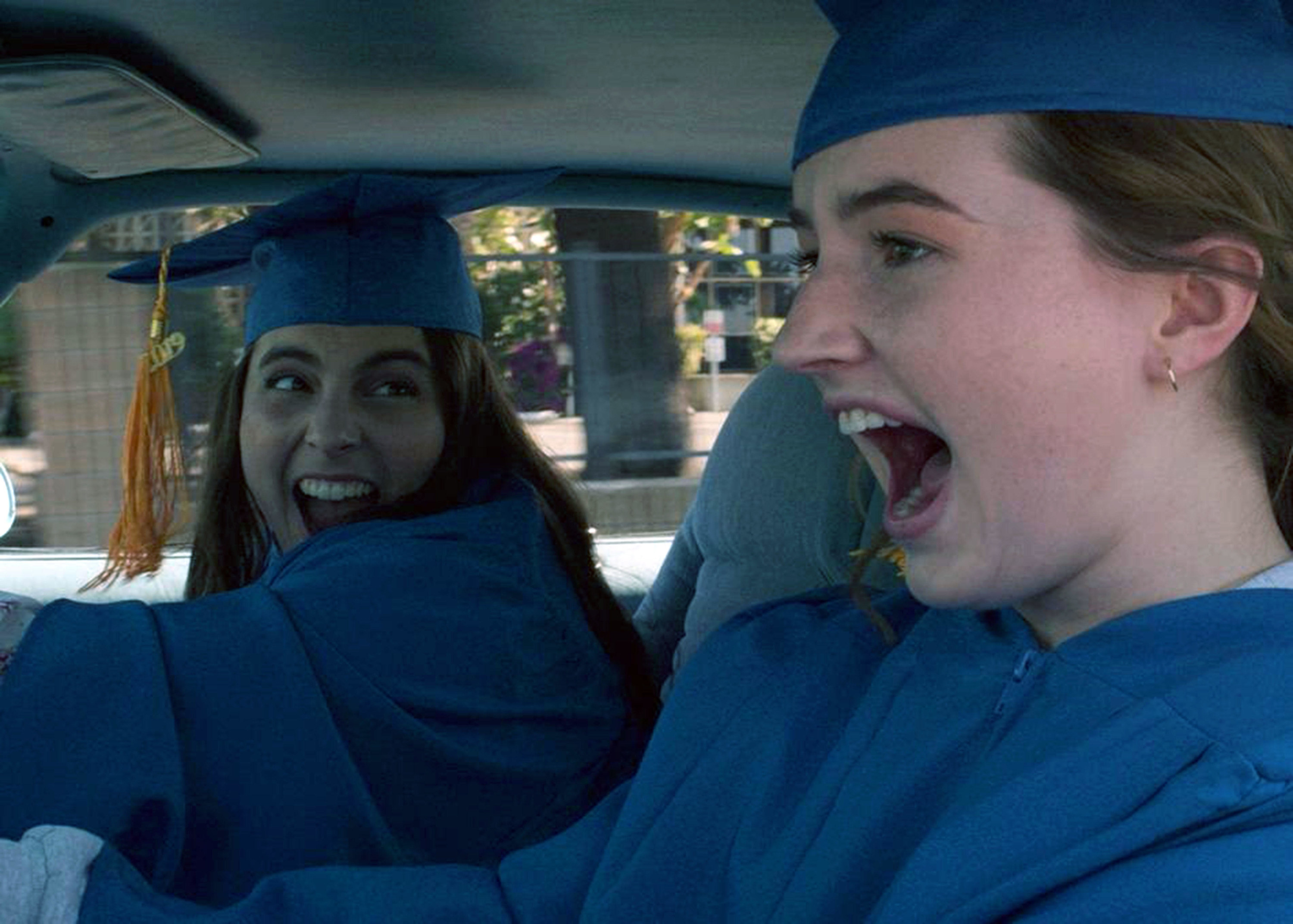 Two young women in graduation gowns scream while speeding to their graduation ceremony