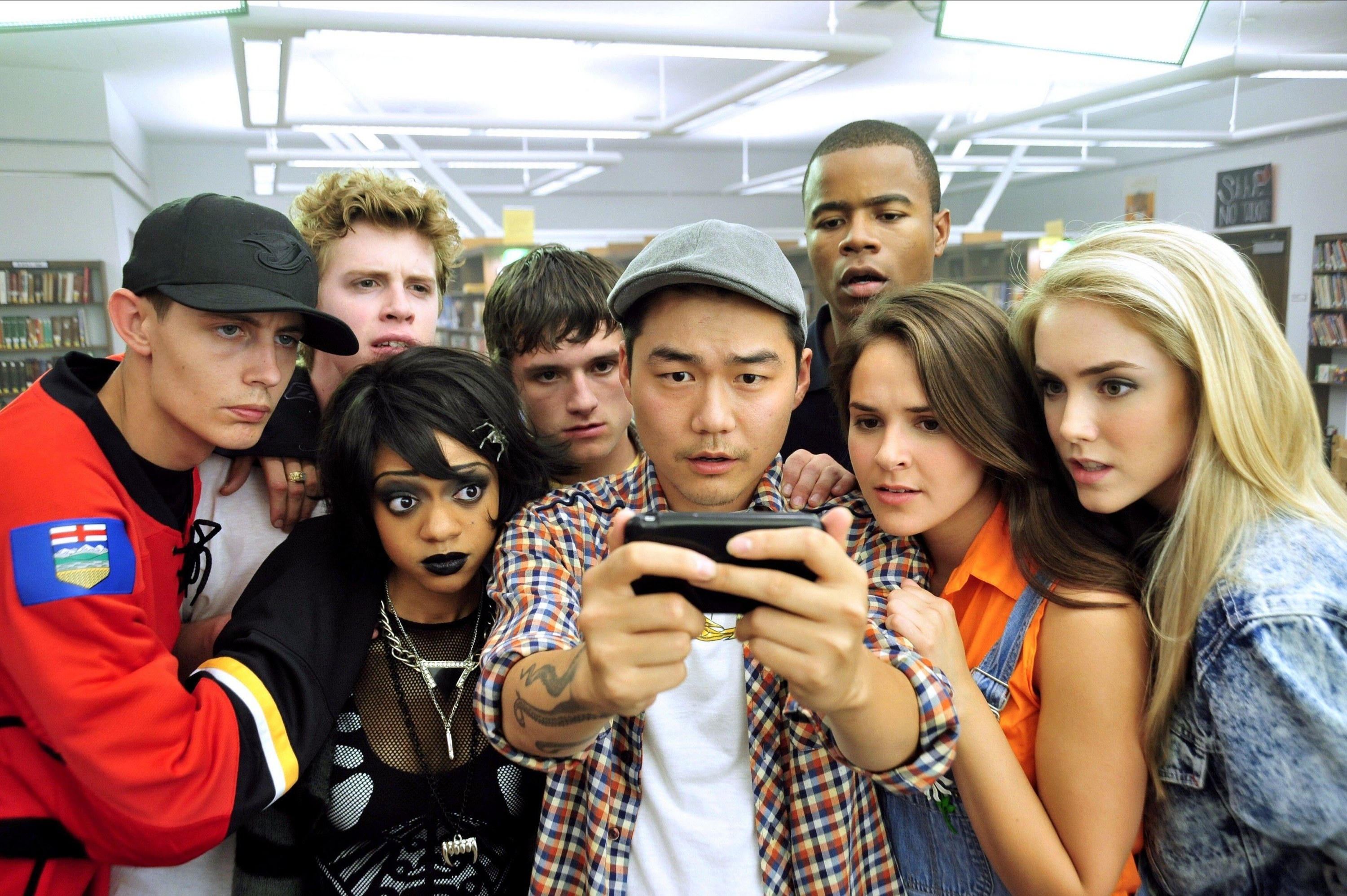 A group of teenagers gather to look at a shocking video on a phone