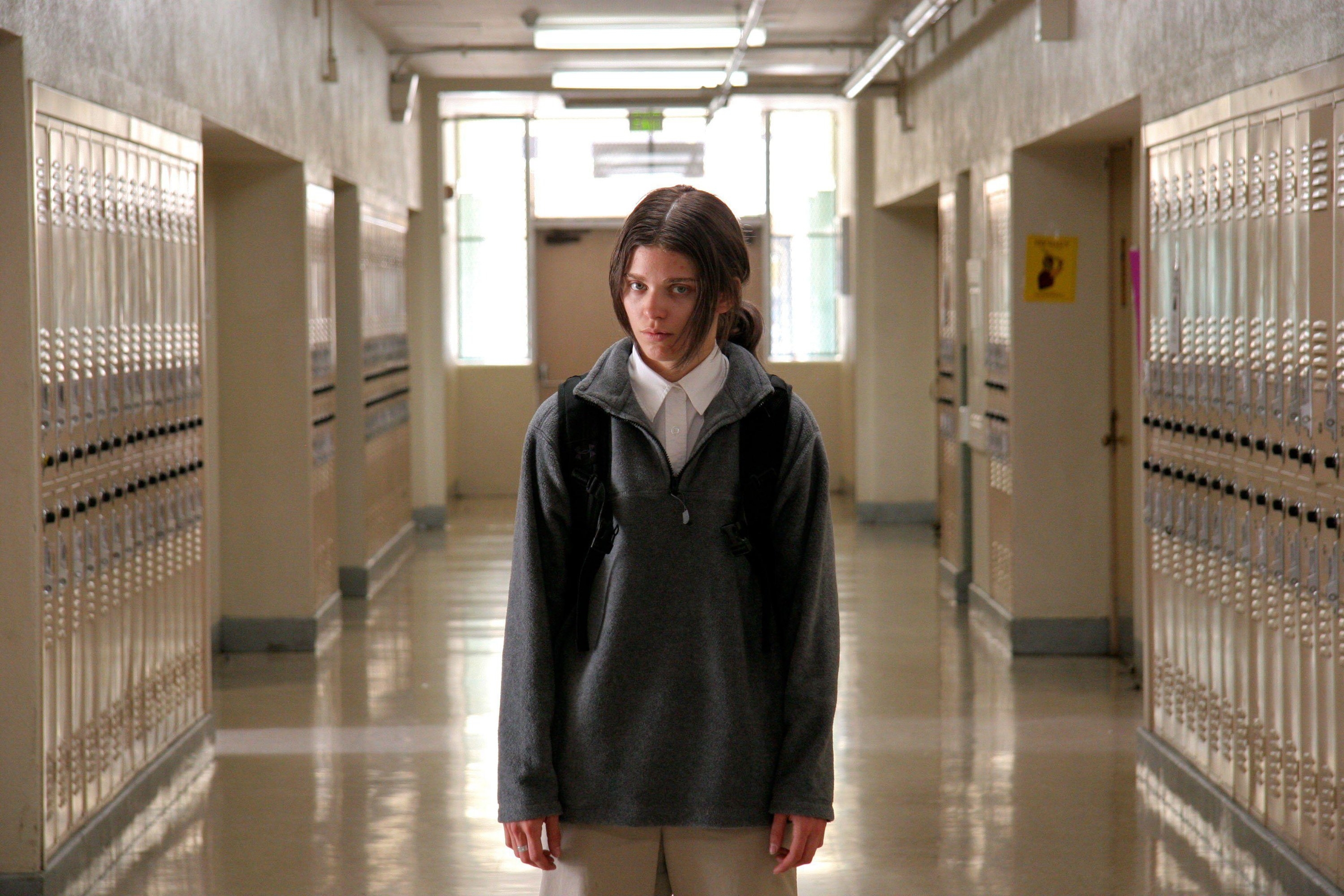 An unnerving young woman stands ominously in a high school hallway