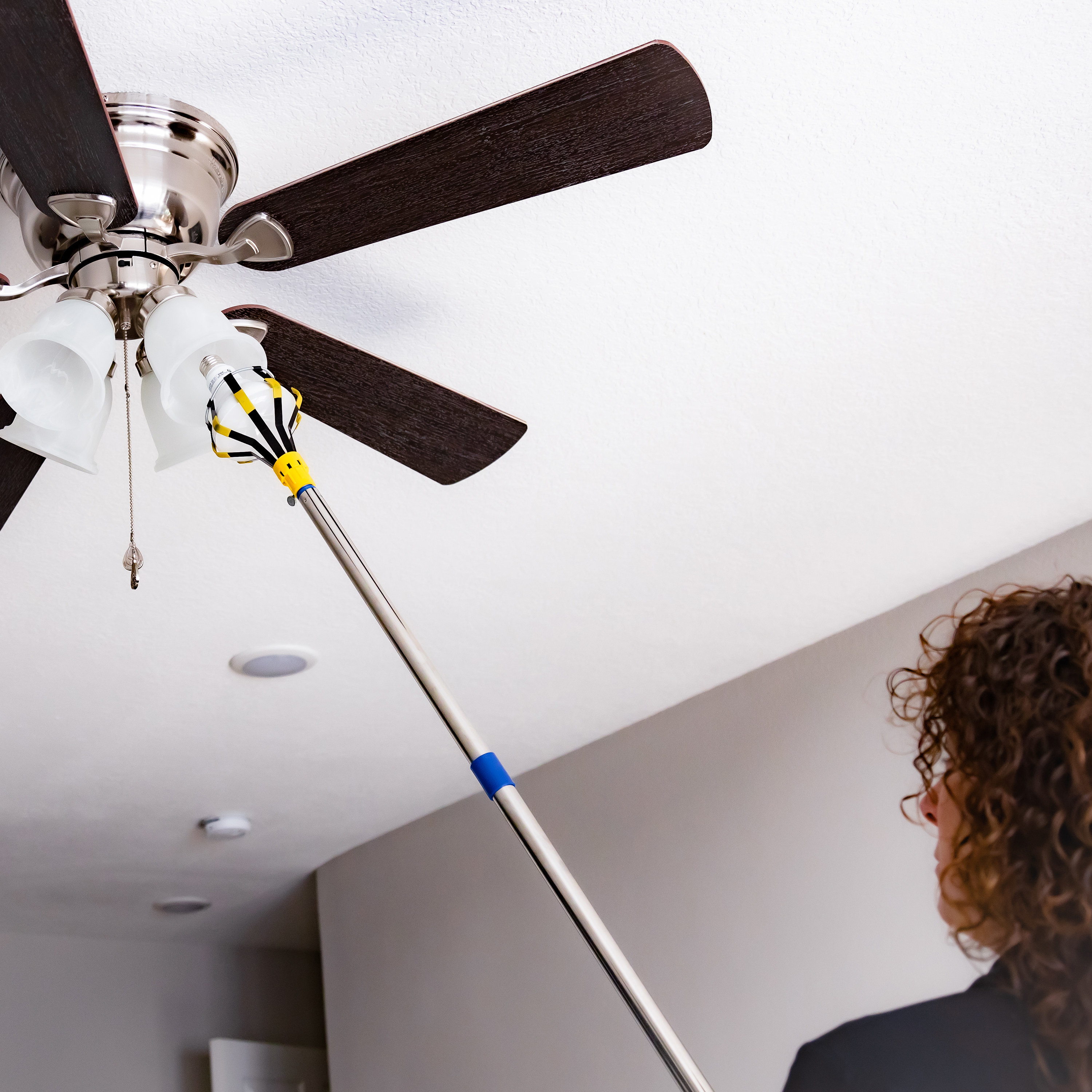 A model using the light bulb changer to change the bulb in a ceiling fan light