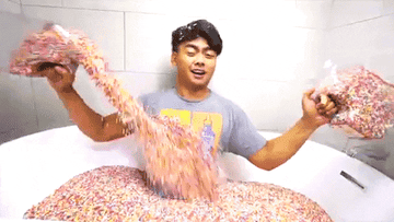 a guy sitting in a bath and pouring sprinkles on himself