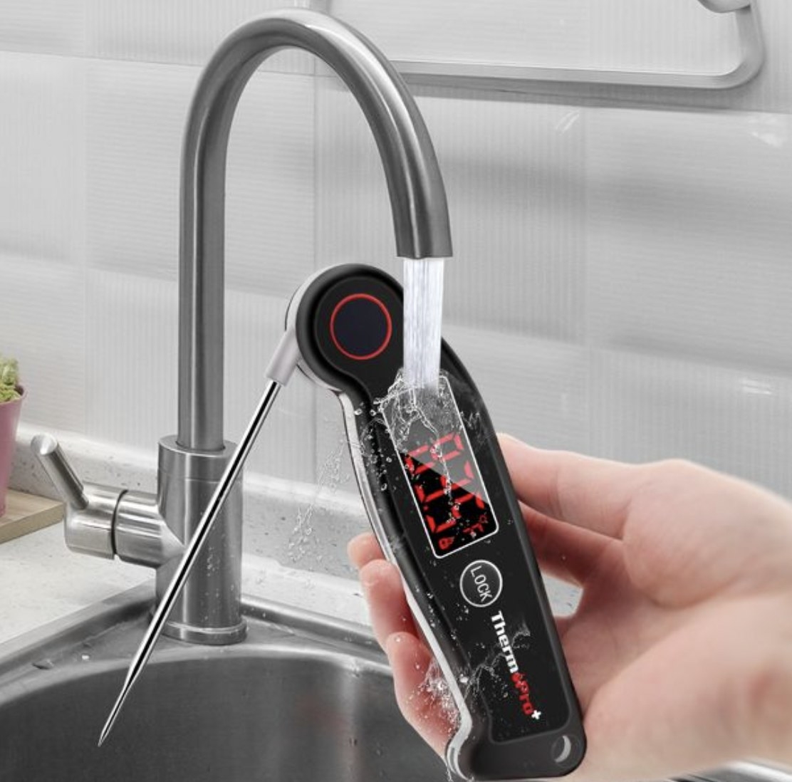A hand holding a digital meat thermometer under a water coming out of a sink