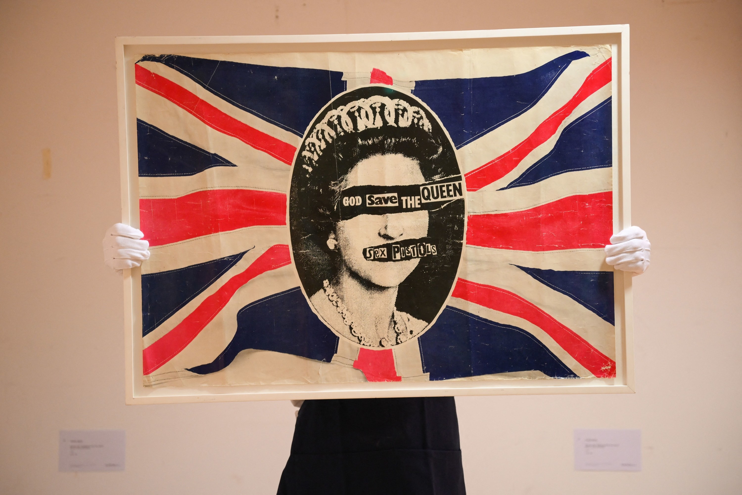 Someone holding a british flag with the sex pistols god save the queen logo in the middle