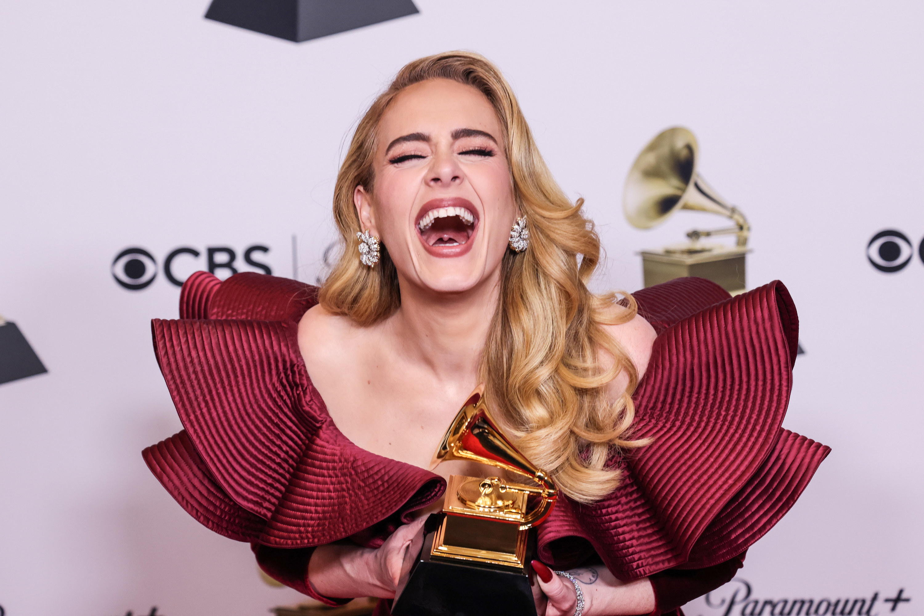 Adele laughing as she holds her Grammy backstage