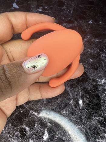 Hand holding orange clitoral vibrator