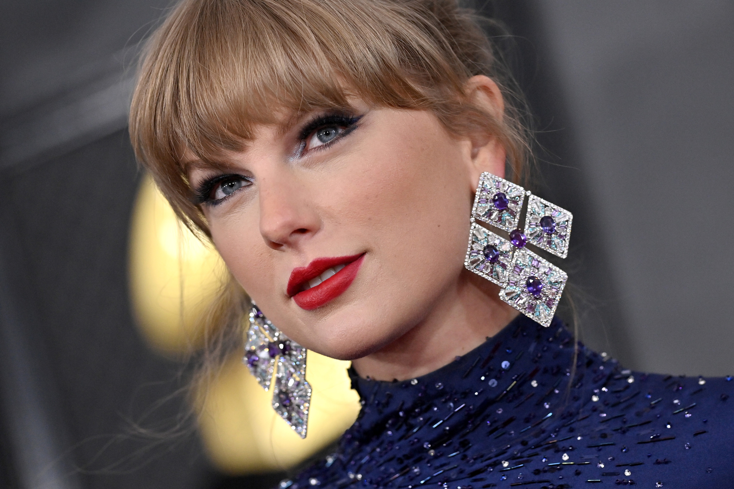 Taylor wears large diamond earrings that consist of four diamond shaped panels held together with a purple sapphire in the middle