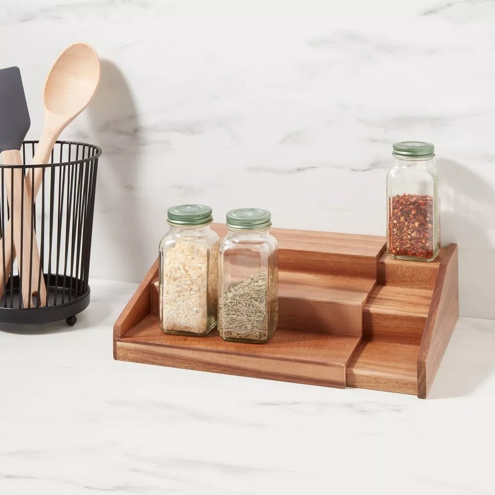 An expandable spice rack with three tiers holding several spices on a kitchen counter