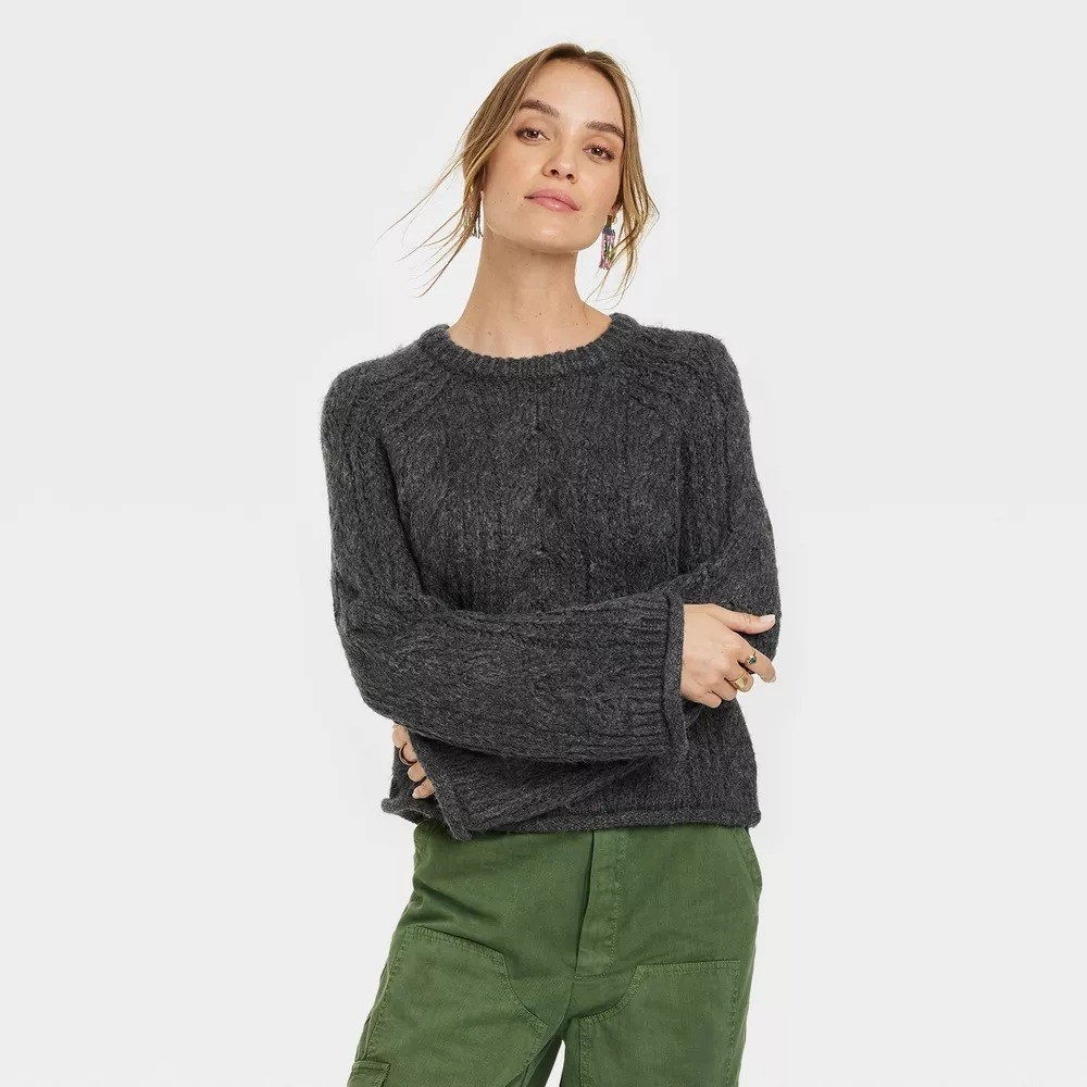 A model in the gray cable knit sweater with green pants