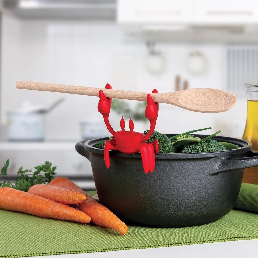 a little silicone crab sitting on the edge of a pop holding a stirring spoon