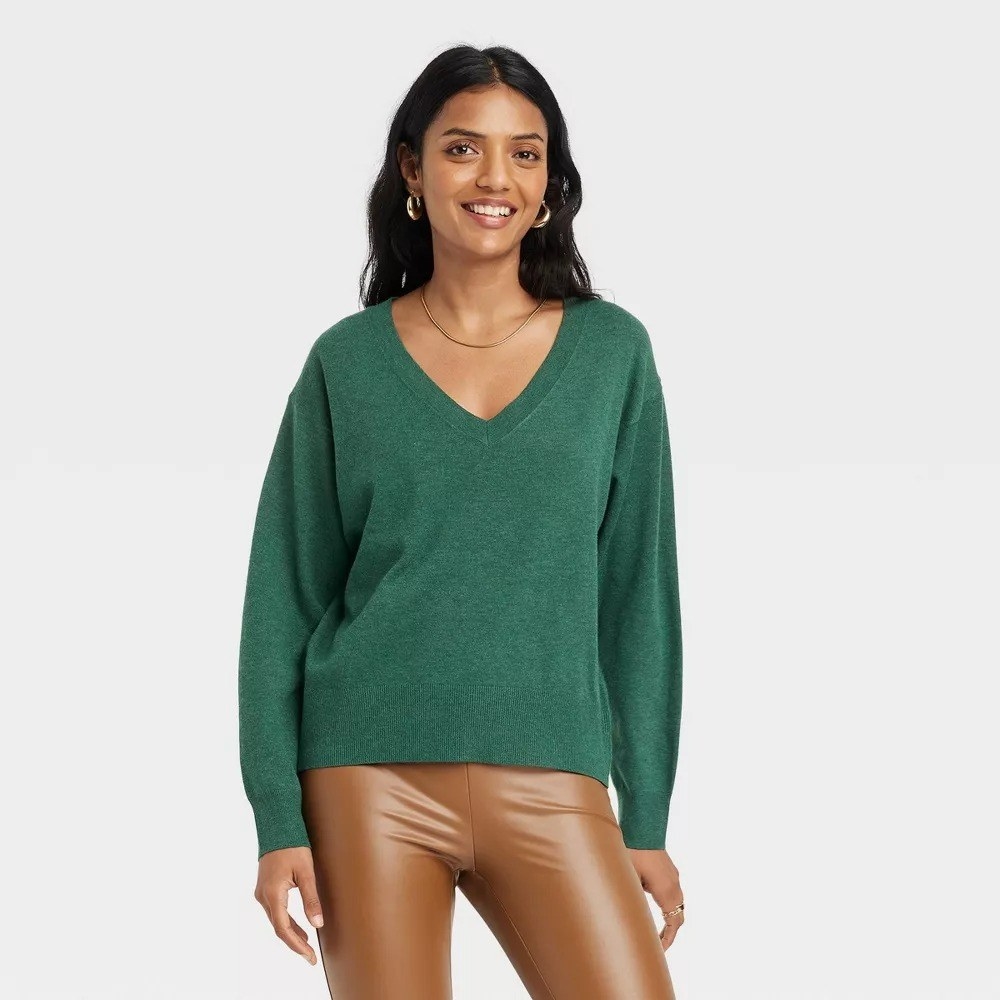 A model wearing the sweater in green with camel leather pants