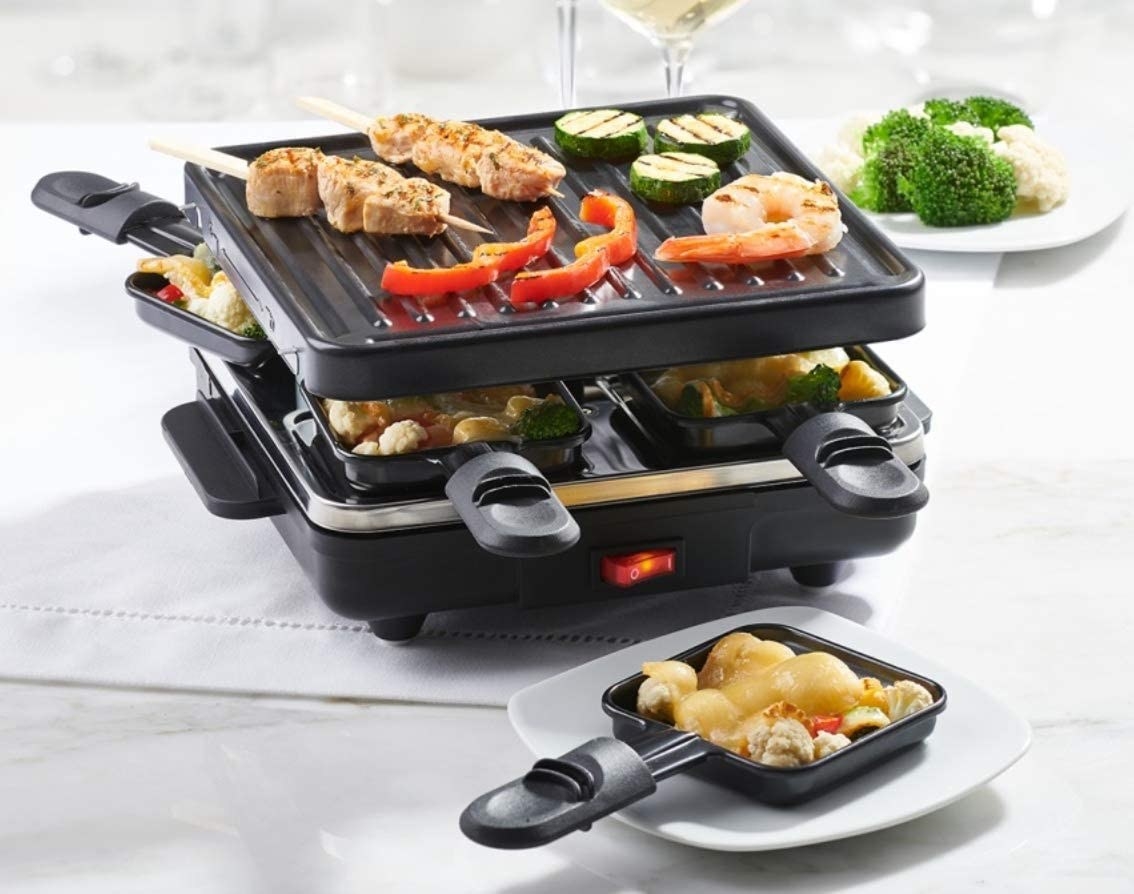 the raclette with some meat and vegetables on top and a warming pan out with cheese on top