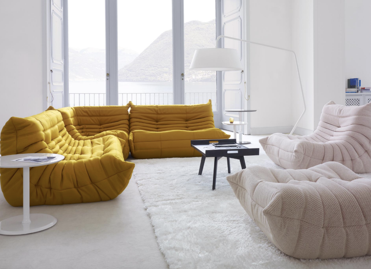Two differently colored Togo sofas in a minimalist living room that leads to a large balcony facing a body of water