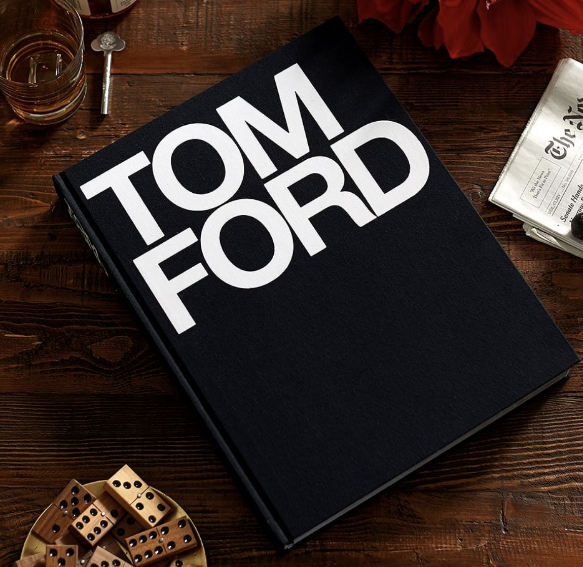 A copy of the large Tom Ford book on a coffee table next to a small bowl of wooden domino pieces and a cocktail