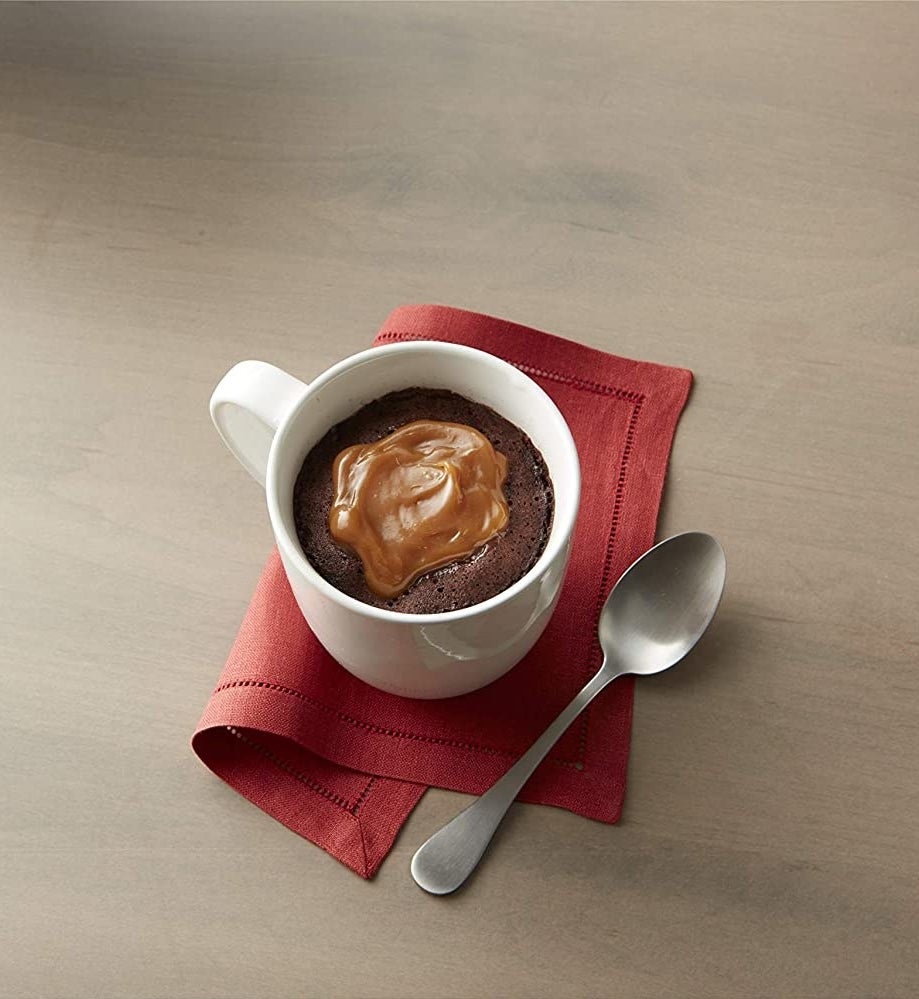 the mug cake in a mug with caramel sauce on it next to a spoon
