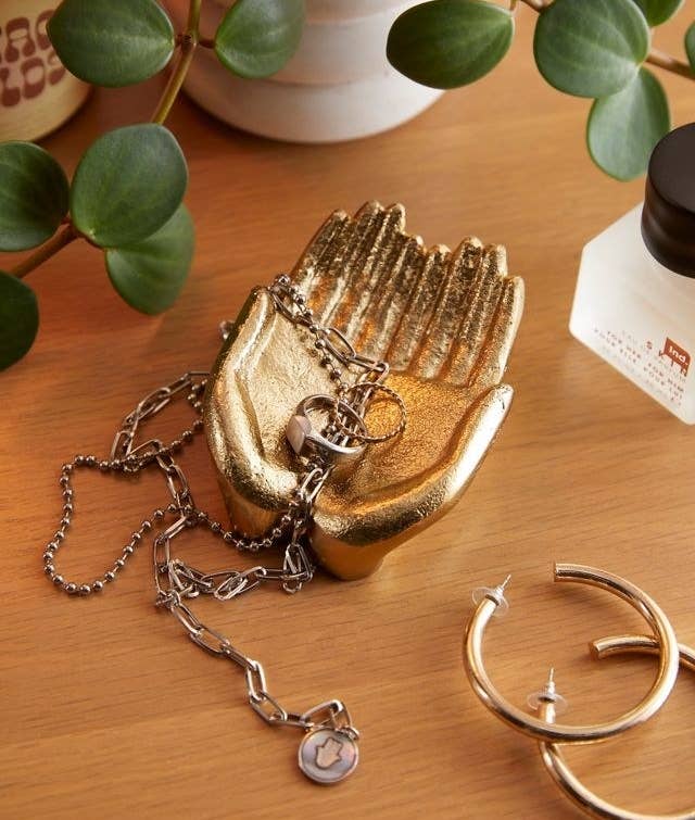 a metallic catch-all dish in the shape of two hands together holding jewellery