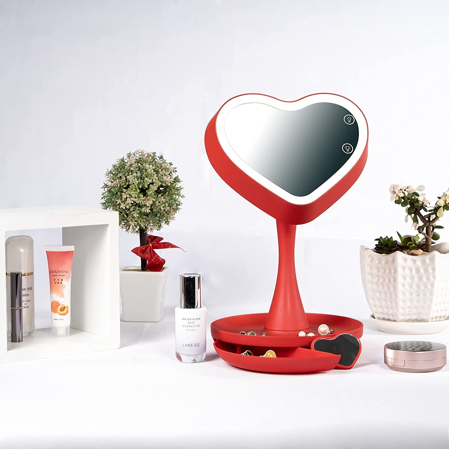 a heart-shaped light-up mirror on a counter surrounded by beauty supplies and plants