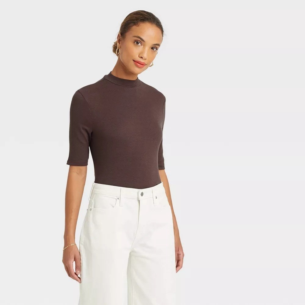 A model wearing the brown mock turtleneck with white pants