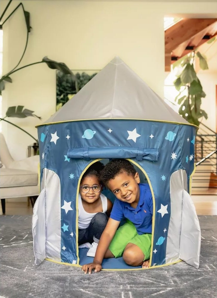 Two child models peaking out of the inside of a blue and white pop-up rocket tent