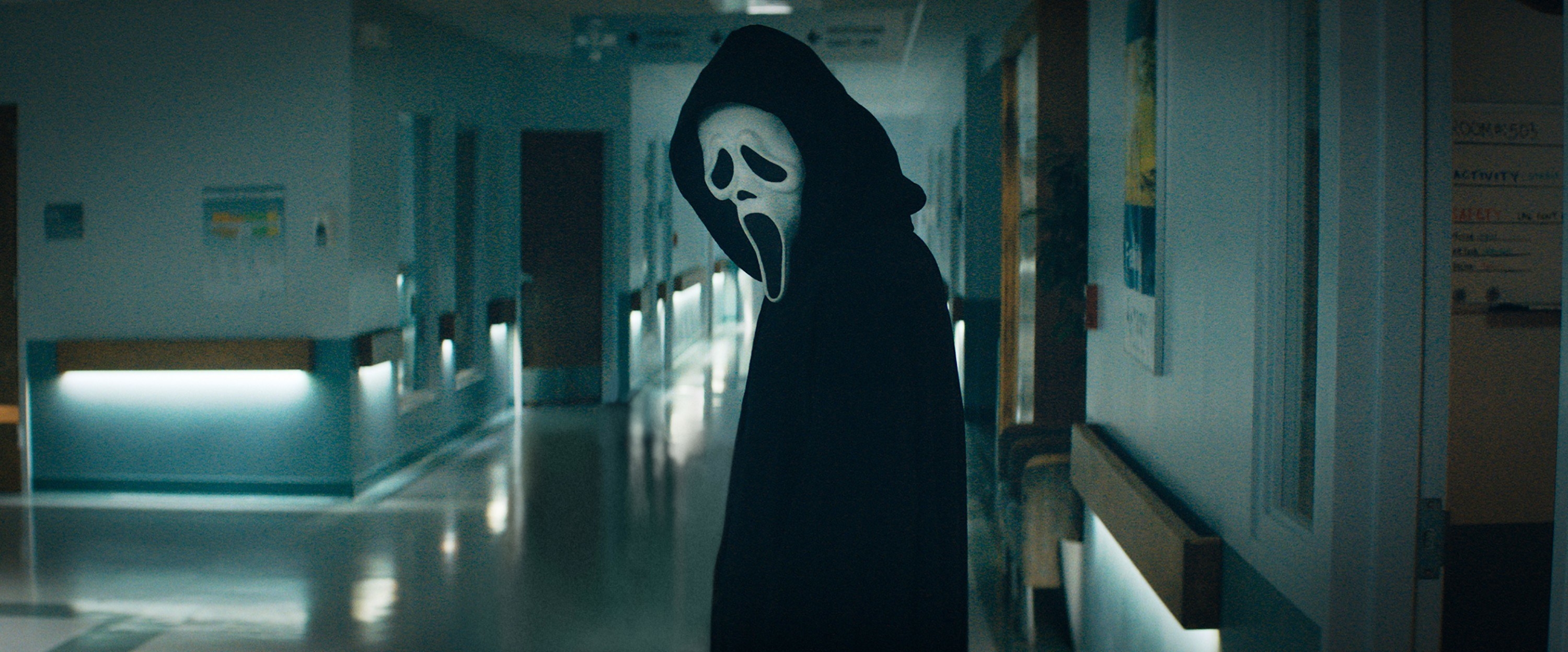 person wearing a scream mask in an empty hallway