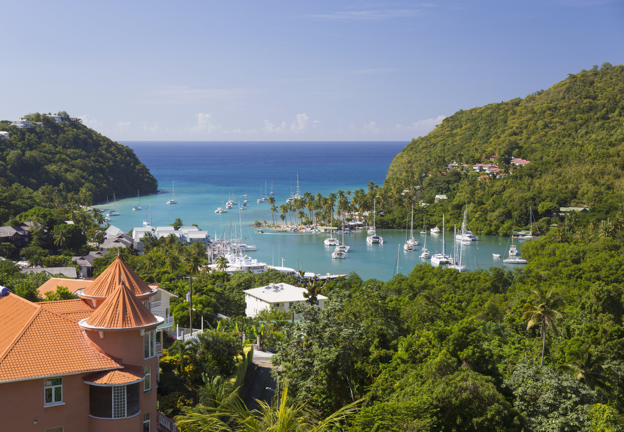 An exotic locale with a resort and trees and boats alongside the ocean