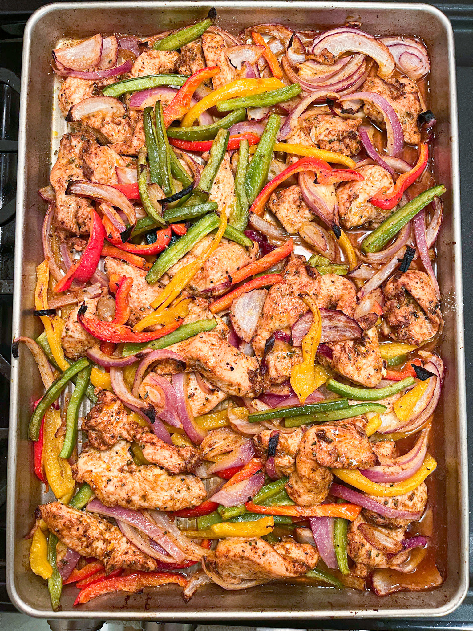 sheet pan with roasted chicken, green and red peppers, and red onion, cooked