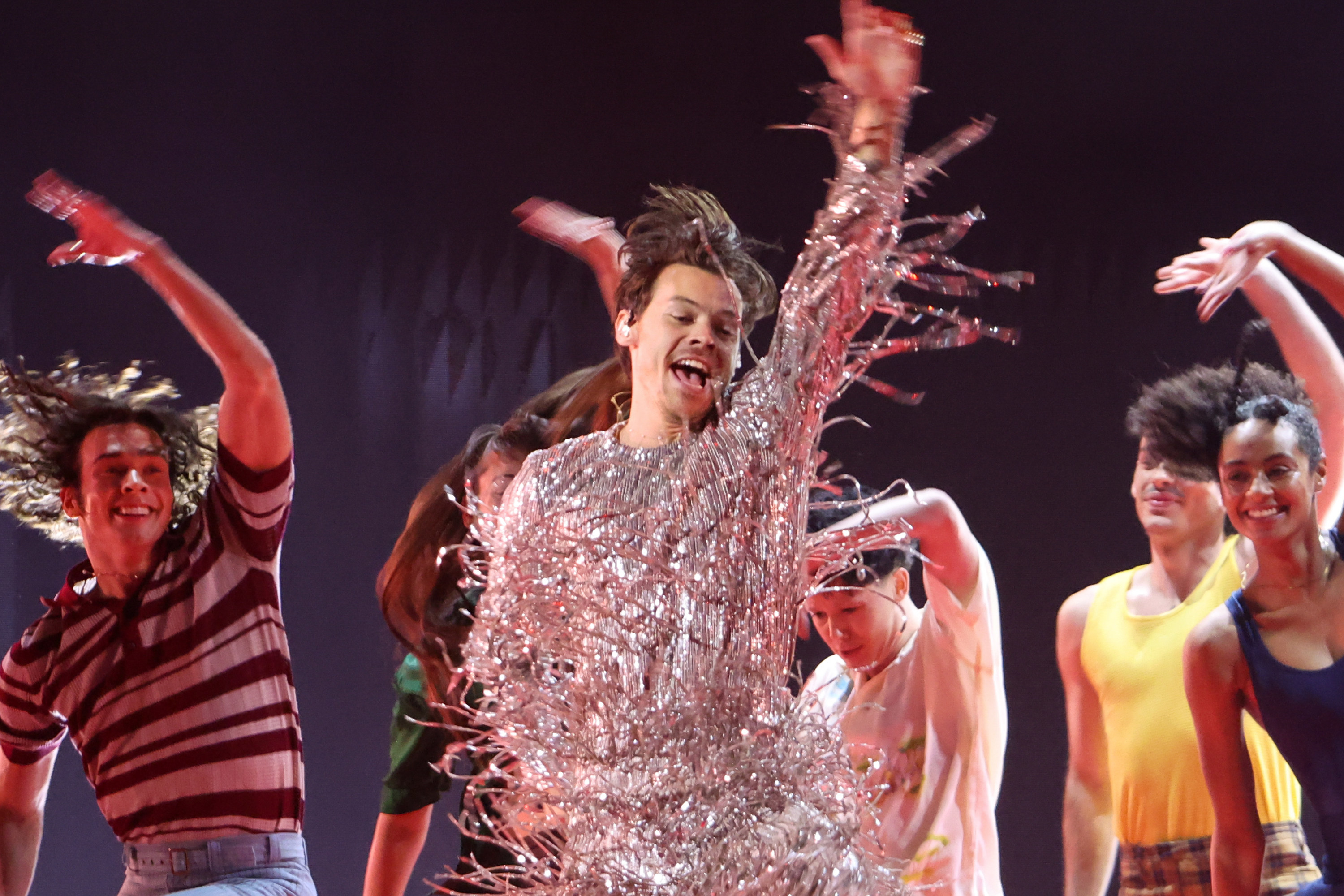 Harry Styles dances with an arm over his head surrounded by dancers mirroring the motion