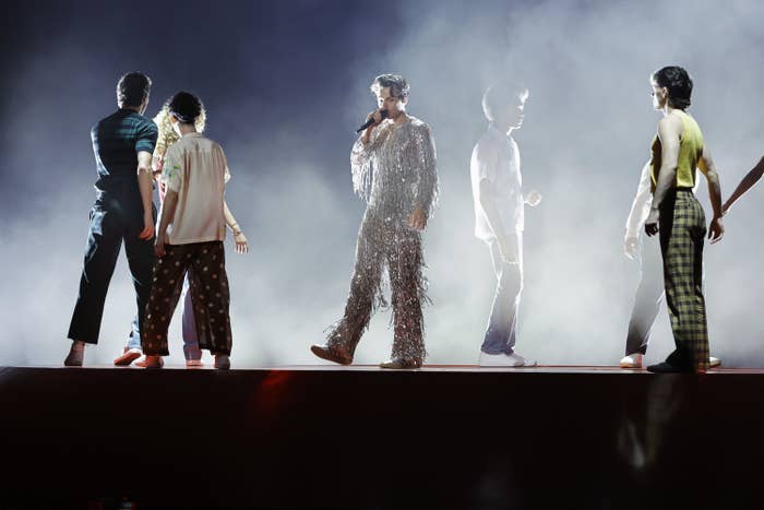 Harry Styles wears a silver quilled body suit on a foggy stage surrounded by dancers