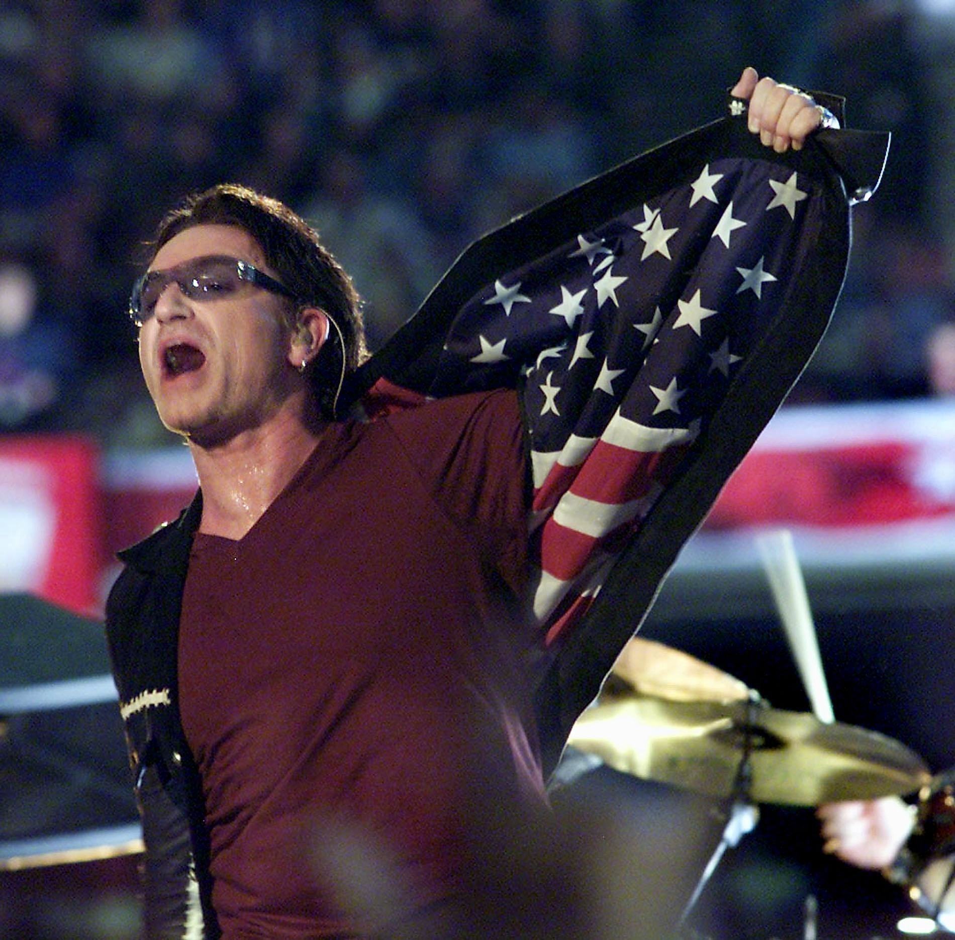 Bono, singer with the Irish rock group U2, opens his jacket exposing an American flag as he performs during halftime 03 February, 2002 of Super Bowl XXXVI