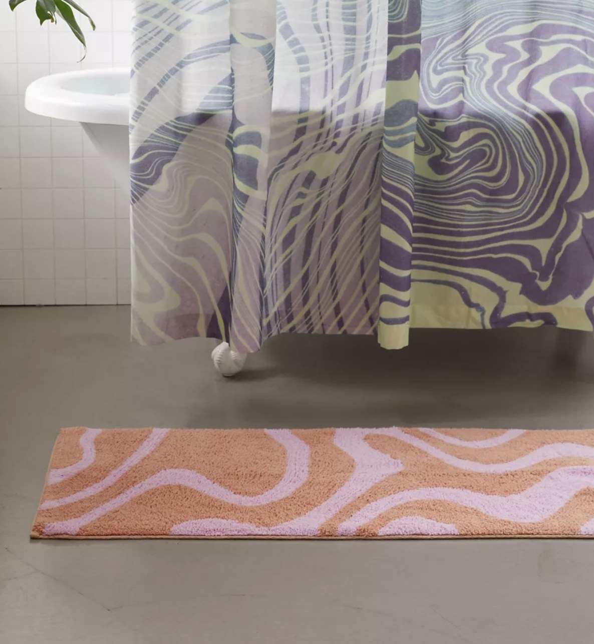 A Pink and orange marble patterned bath mat in front of a tub with a shower curtain
