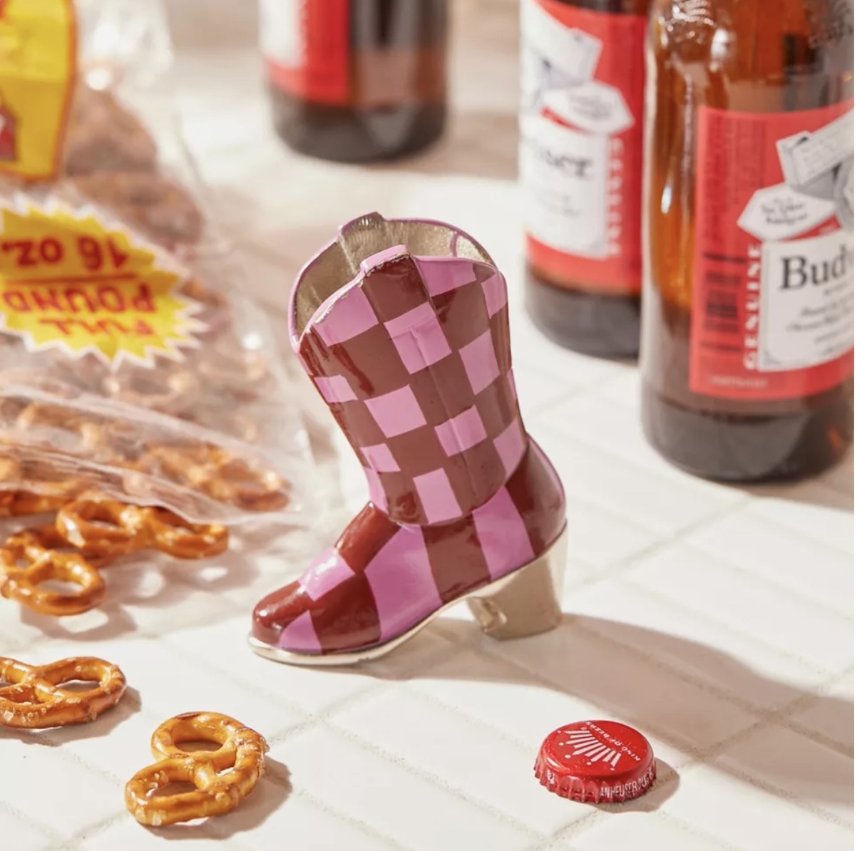 A boot-shaped bottle opener next to an open bag of pretzels and a few bottles of beet