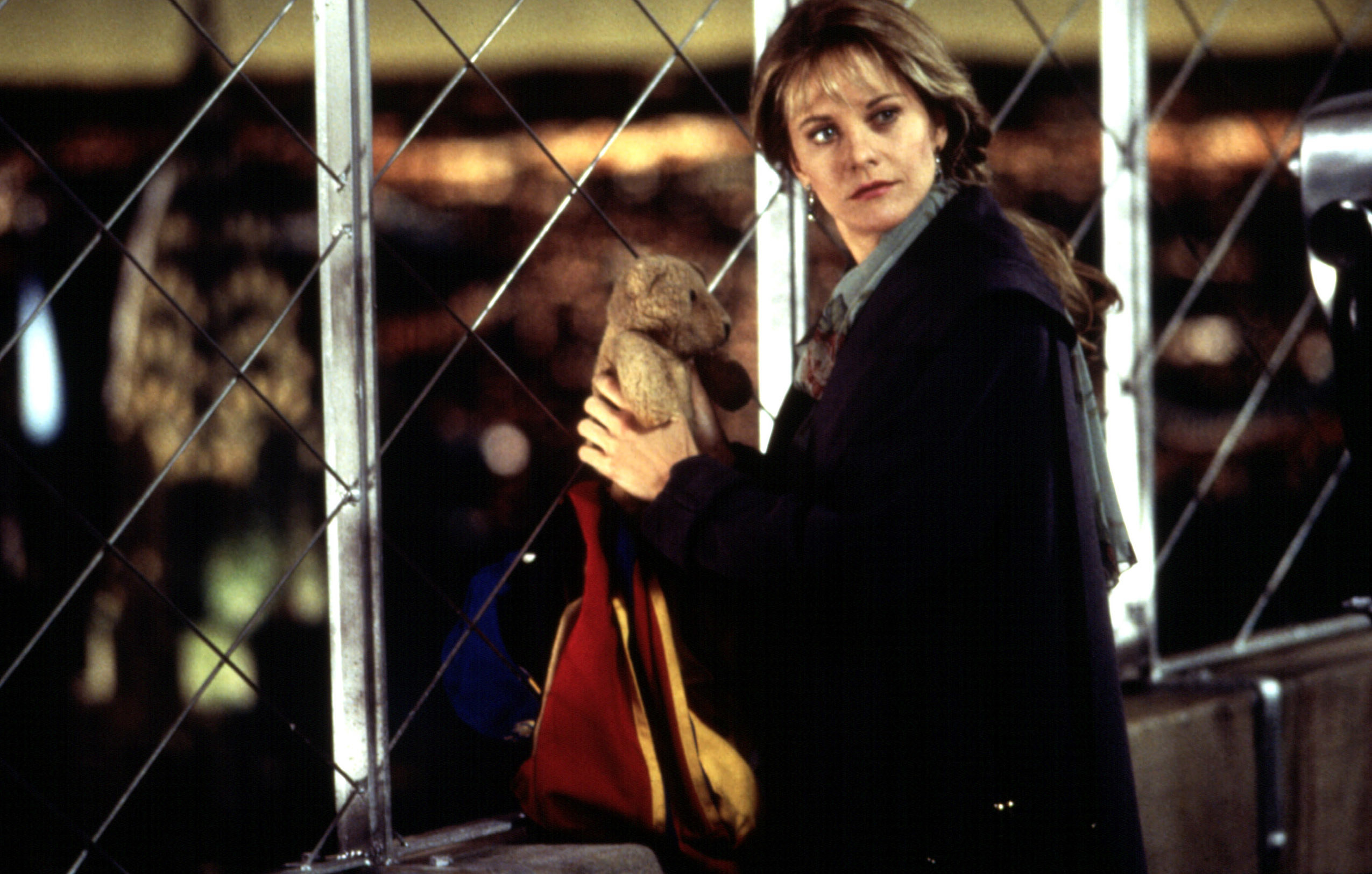 A woman holds a teddy bear, looking back at someone off screen