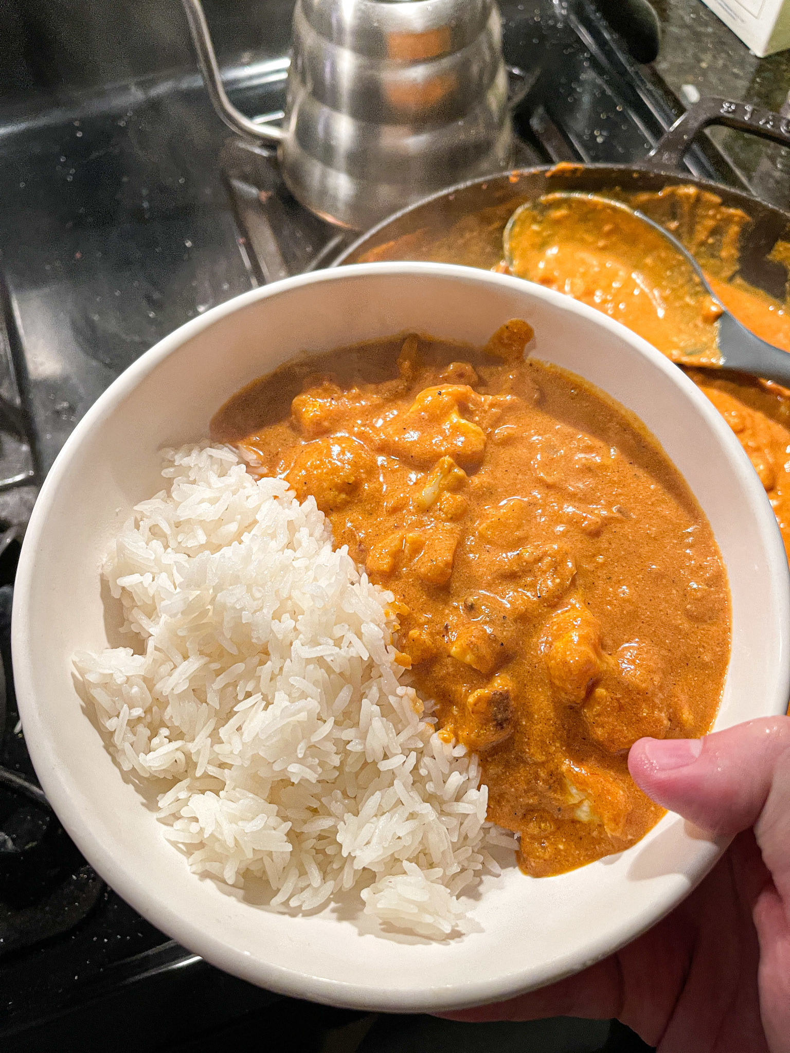 author holding bowl that&#x27;s half steamed rice and half an orange curry with cauliflower