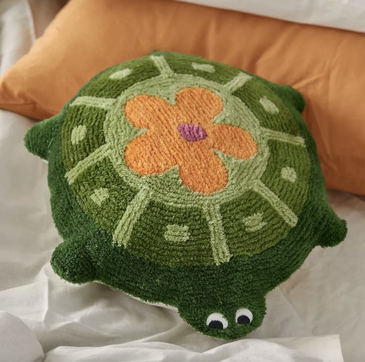 A green turtle-shaped throw pillow with an orange flower design on it