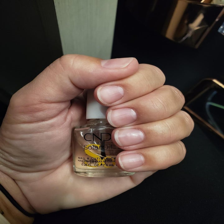 reviewer with strong-looking nails holding bottle of the cuticle oil