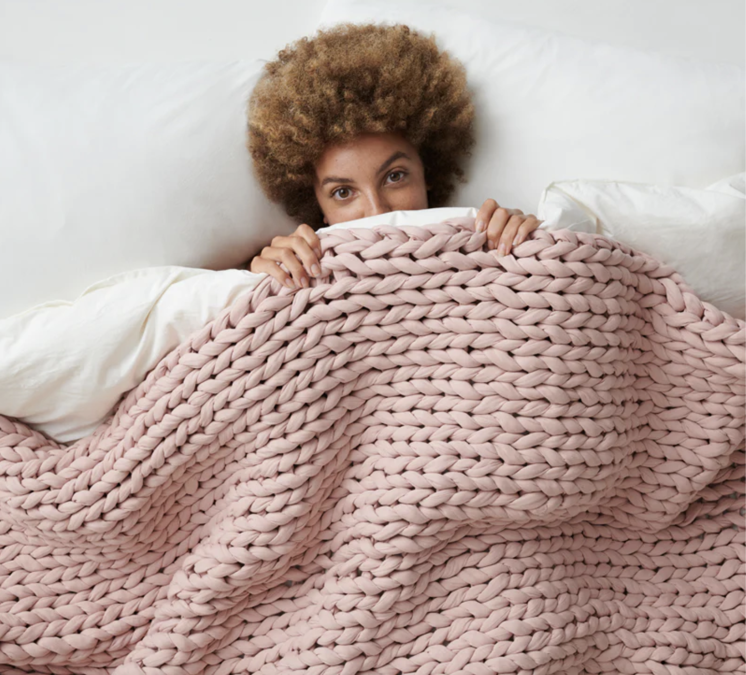 A model lying under the pale pink blanket in bed