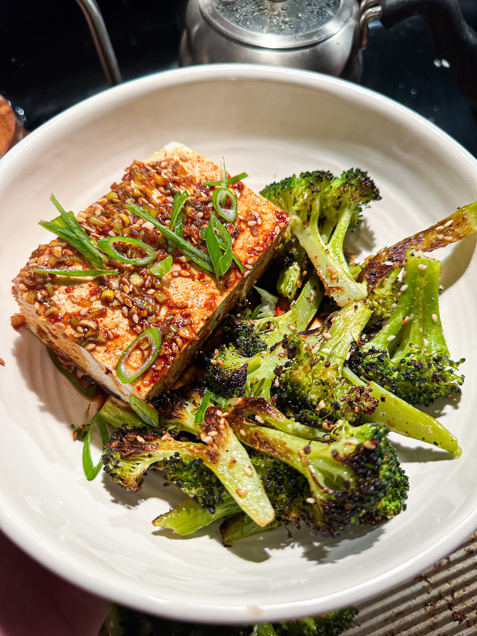 block of tofu next to roasted broccoli, with a brown sauce with sesame seeds drizzled overtop