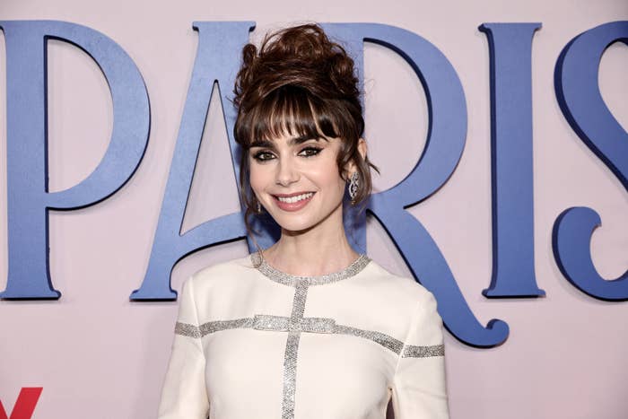 Lily smiling at a red carpet event. Her hair is in an updo that shows off her bangs