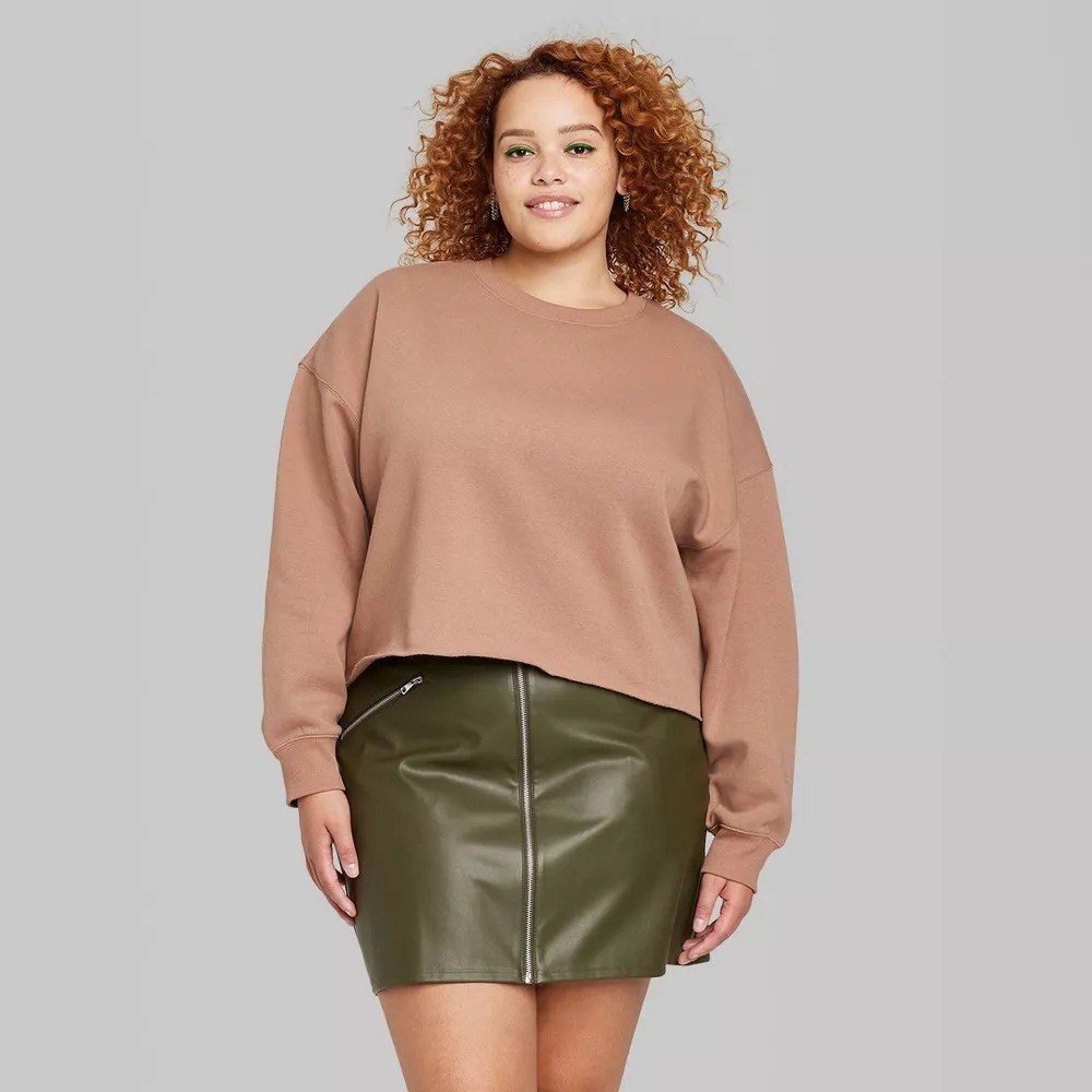 a model wearing the tan cropped sweater with a green skirt