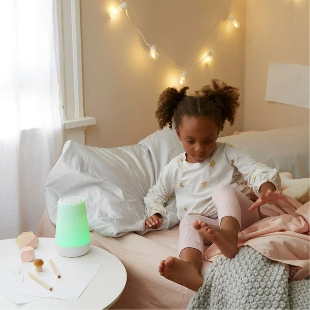 a child getting out of bed with the night light sound machine on a table next to the bed