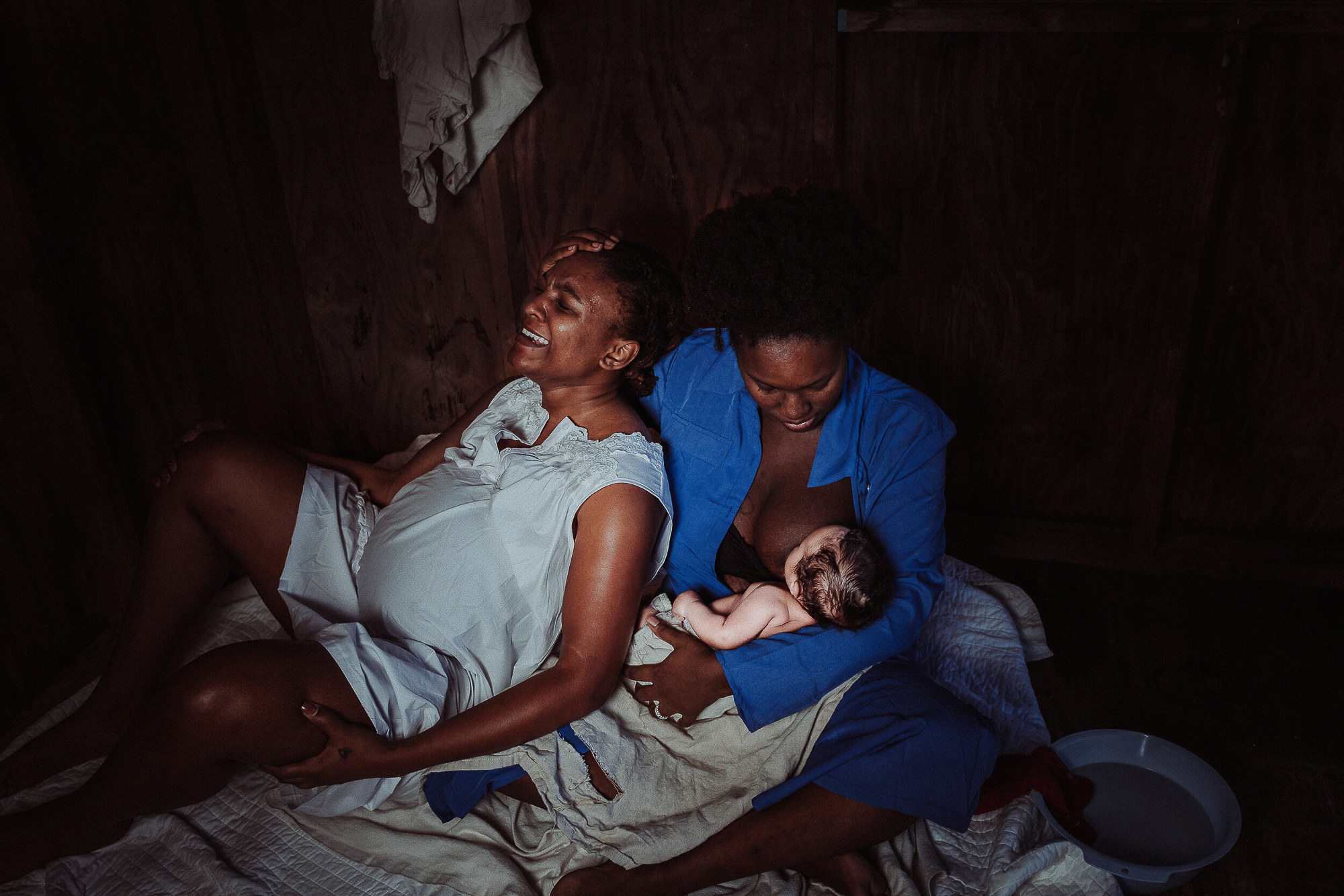 An image of a Black doula holding a newborn, next to a Black mother