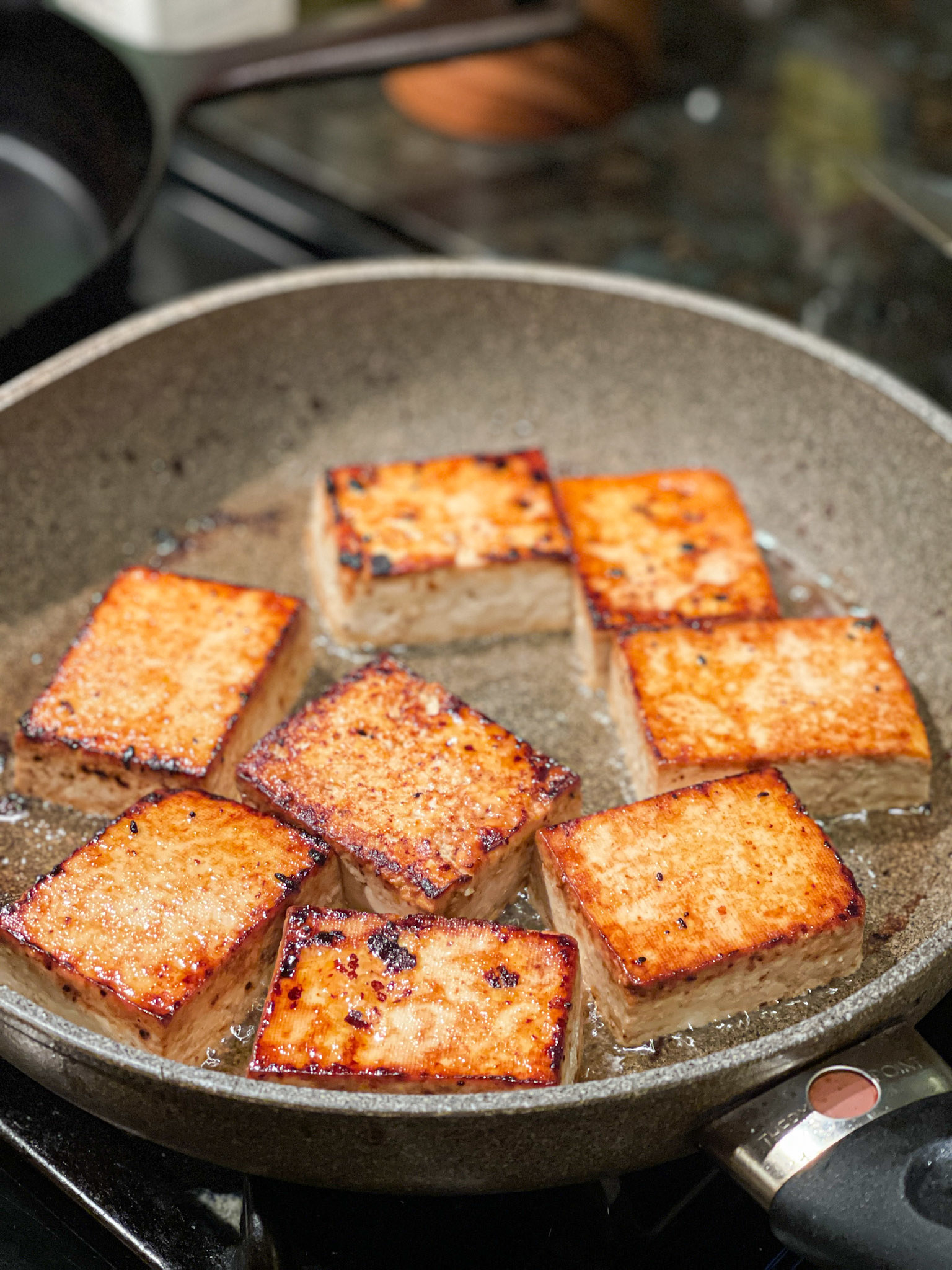 slices of tofu in a nonstick skillet that are frying on one side and golden brown and crispy on the other