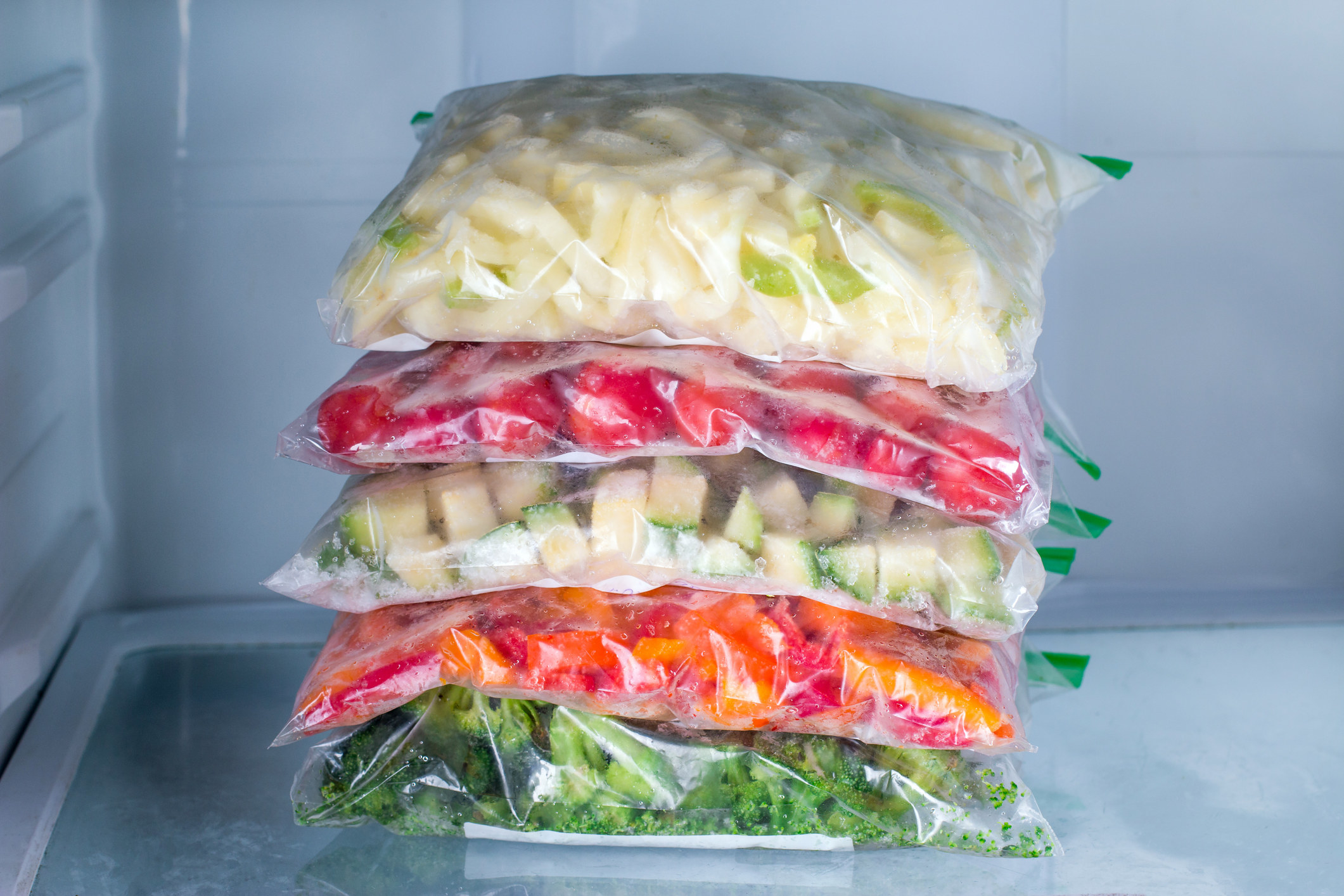 Bags with frozen vegetables in freezer.