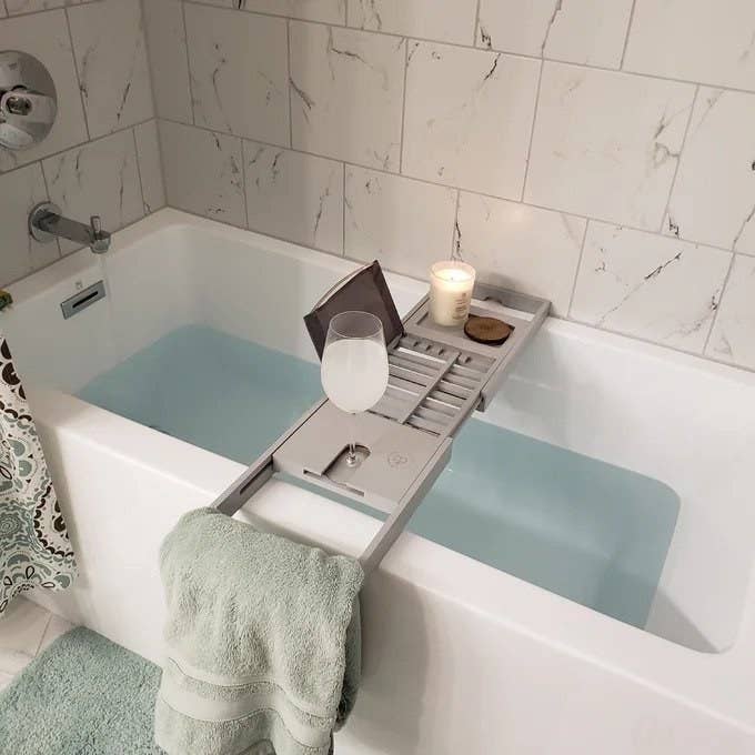 Gray bath tray over white tub, wine glass, candle and iPad on tray