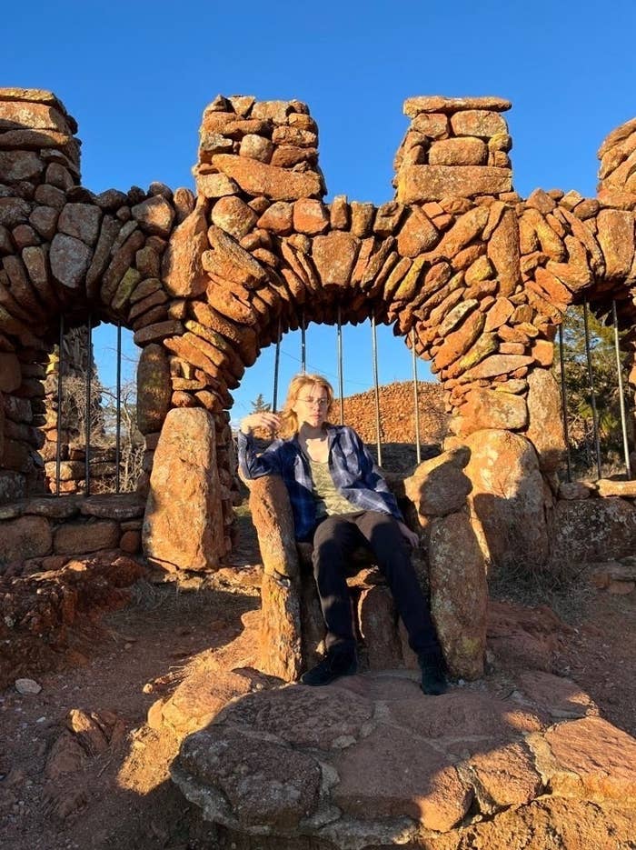 A person sits in a rock formation resembling a chair outside